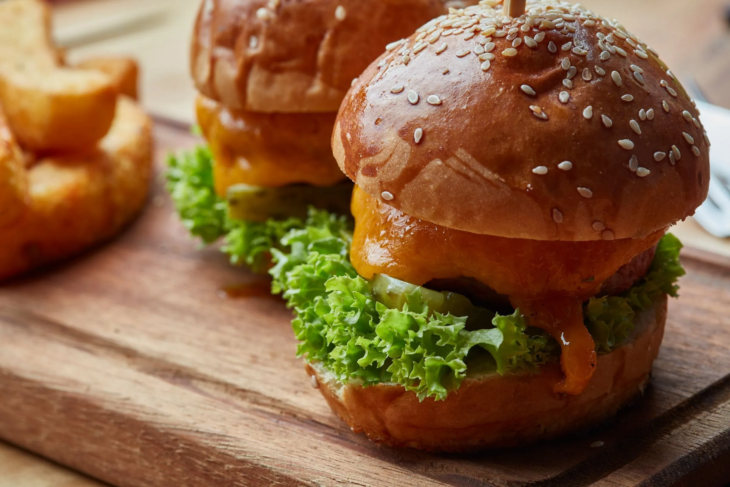 Burgers garnis de salade et de fromage fondu sur une planche en bois