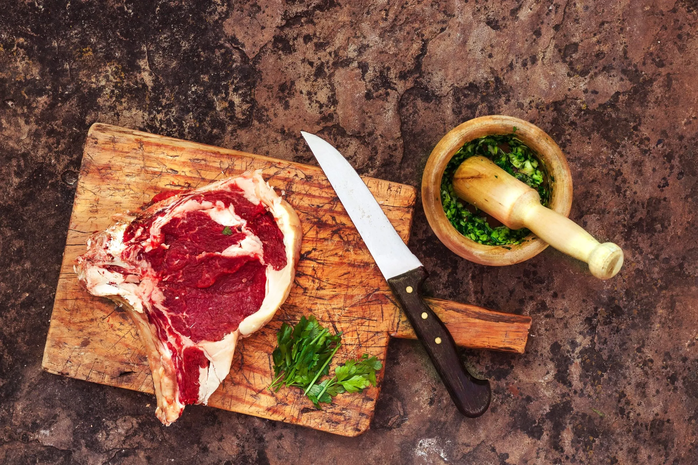 Côte de bœuf crue sur une planche, couteau et herbes fraîches